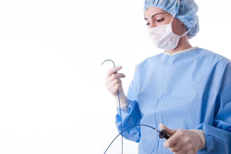 female surgeon in blue scrubs holding catheter